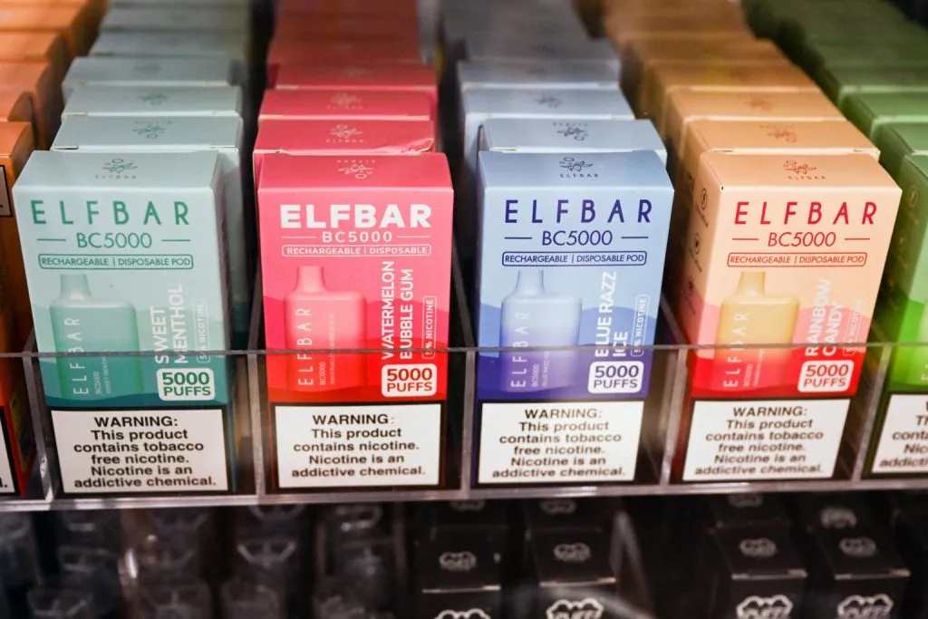 Shelf display of ELF BAR BC5000 vape boxes featuring Sweet Menthol, Watermelon Bubble Gum, Blue Razz, and Rainbow Candy flavors, each offering 5000 puffs.