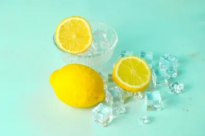 Limón fresco entero y en rodajas junto a cubos de hielo sobre fondo turquesa.