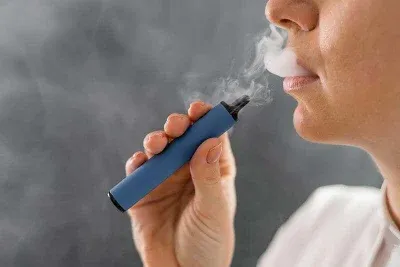 Persona utilizando un vape azul exhalando vapor en el aire.