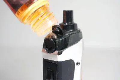 Nahaufnahme eines Vape-Geräts, das mit einer Flüssigkeit aus einer Flasche nachgefüllt wird.